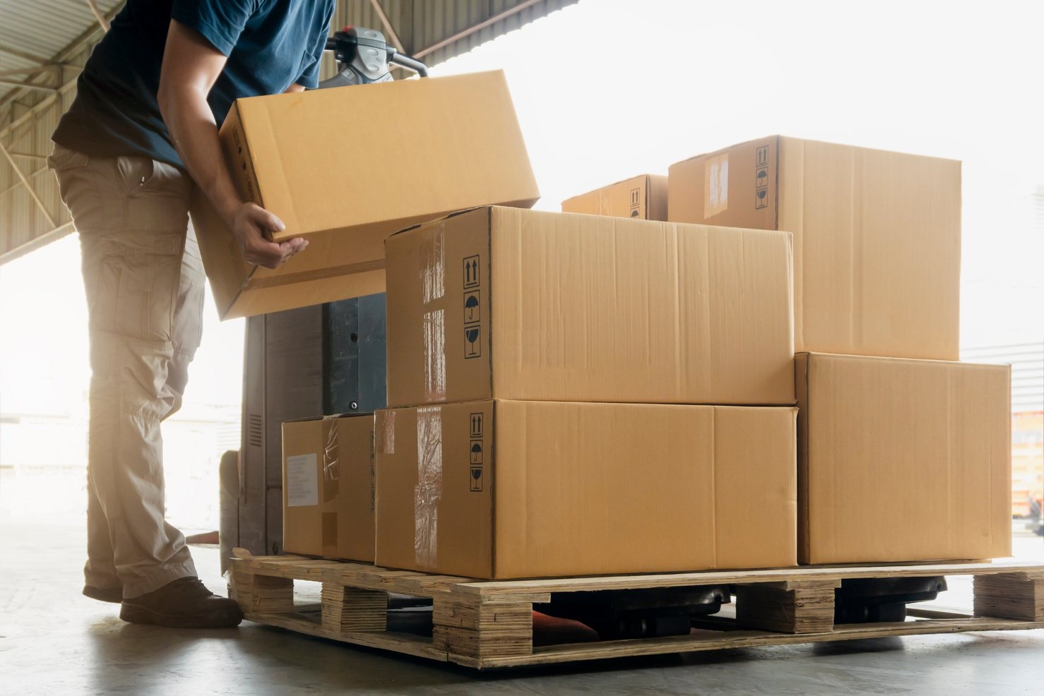 Worker courier lifting shipment boxes stacking on pallet.